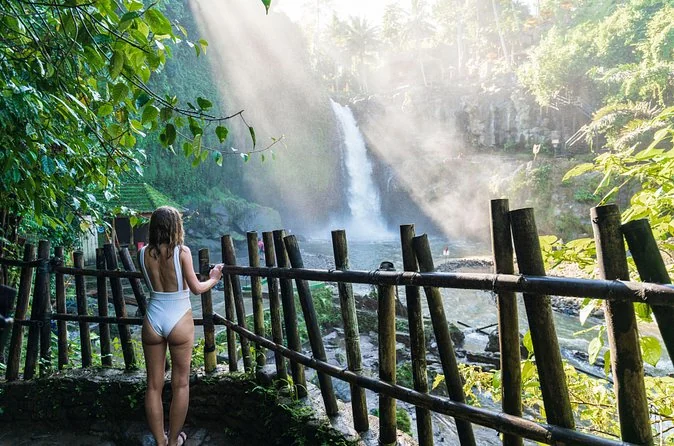 A woman standing behind a bamboo fence beside a waterfall