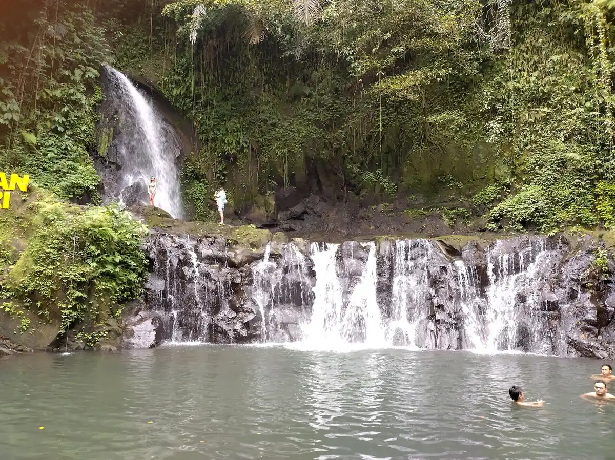 A wide stepped waterfall with swimmers in the pool below